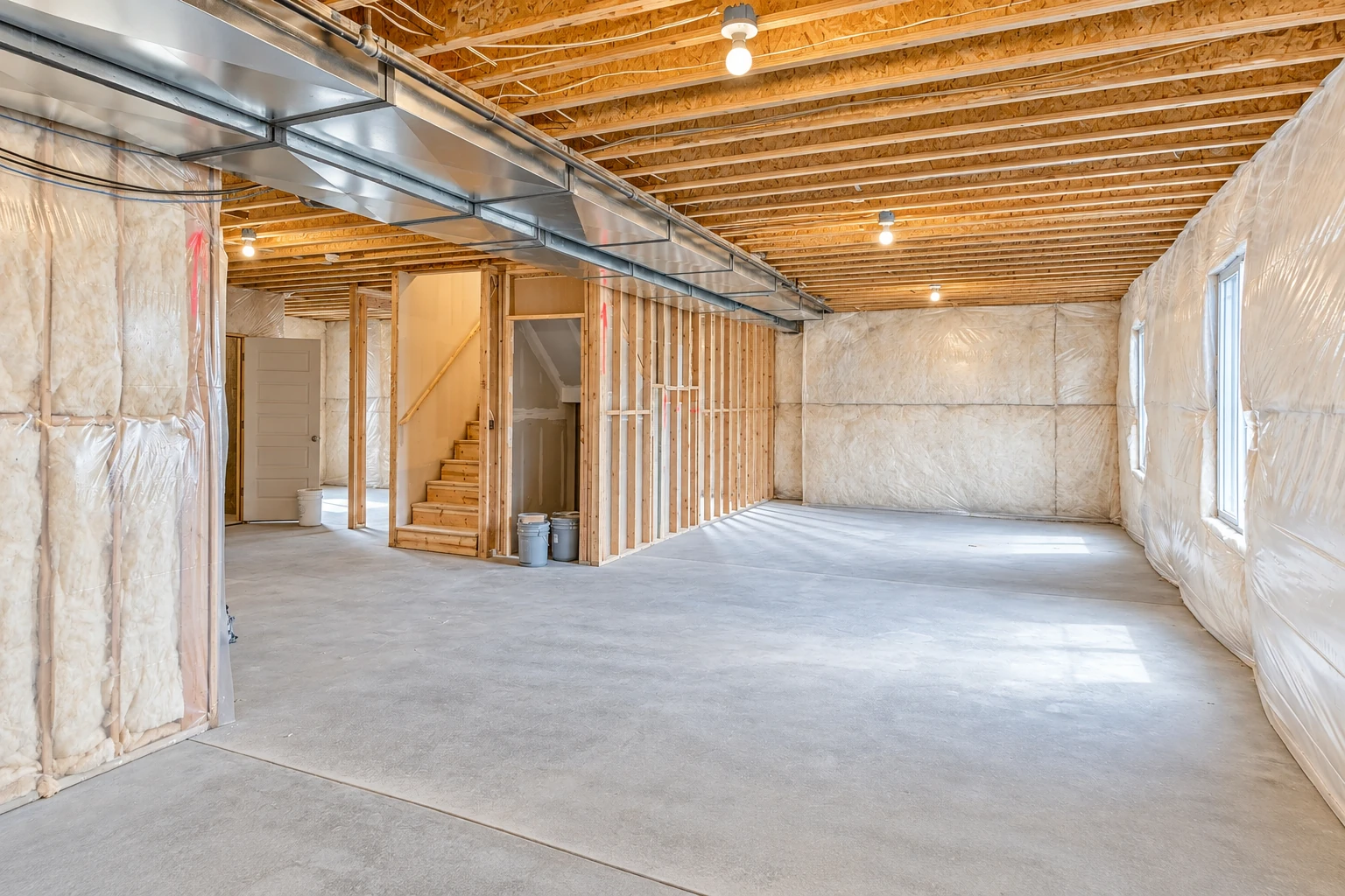 Unfinished basement with fiberglass insulation along the walls, exposed ceiling joists, and a metal air duct.