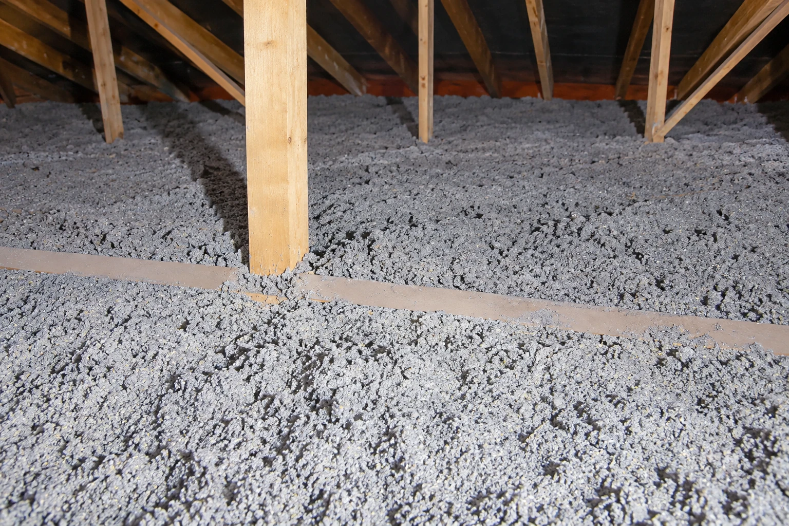 Gray blown-in insulation blankets an attic floor around exposed wooden supports.