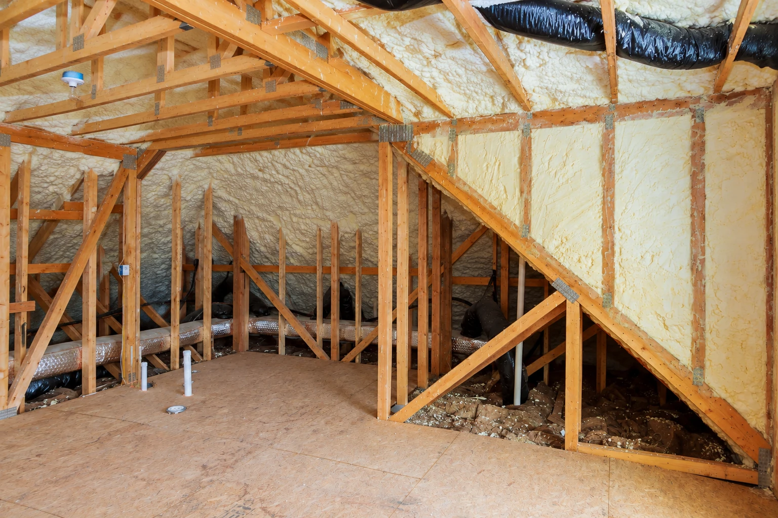 Yellow closed-cell foam insulation covers the roof and walls of a timber attic with exposed framing and ducts.