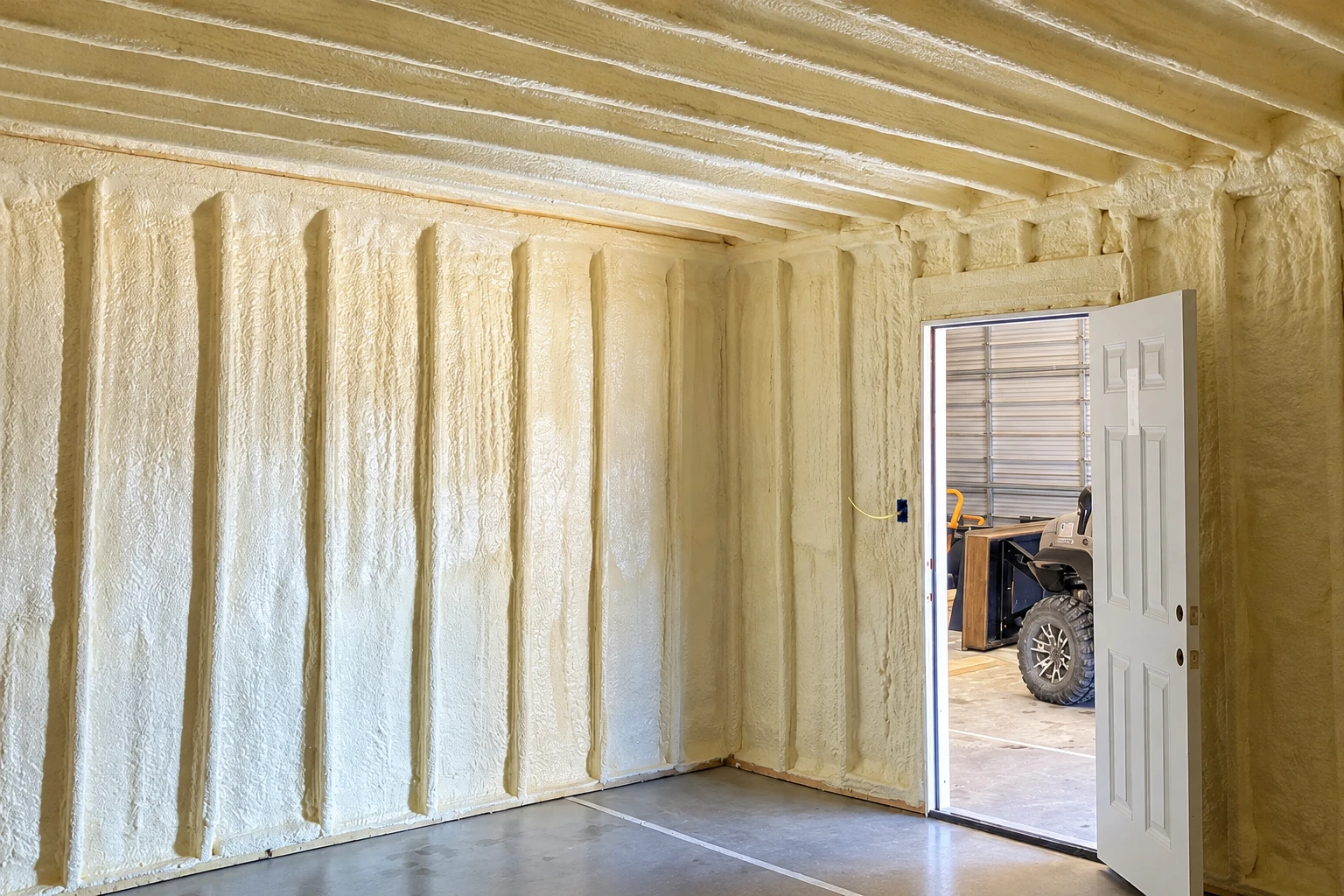 Commercial garage interior with cream spray foam insulation covering the walls and ceiling around the exposed framing.
